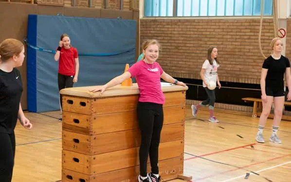 Sportunterricht in der Turnhalle, eine Schülerin lehnt an einem Kasten