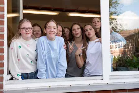 Eine Gruppe Schülerinnen winkt aus einem offenen Fenster