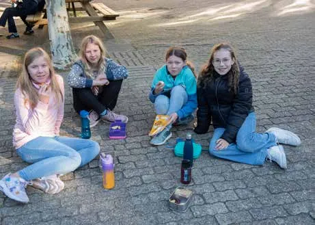 Vier Schülerinnen sitzen beim Frühstück auf dem Pflaster des Schulhofs