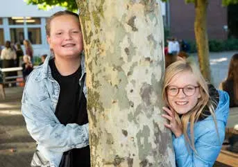 Zwei Kinder schauen hinter einem Baum hervor