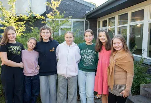 Sieben Schülerinnen stehen nebeneinander vor dem Schulgebäude